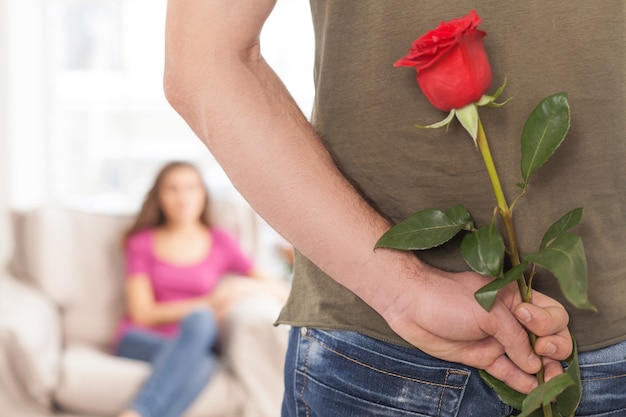 Bloem voor haar. bijgesneden afbeelding van man met een rode roos terwijl zijn vriendin op de achtergrond zit