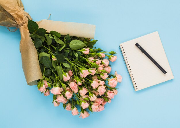 Gratis foto bloemen boeket; spiraal blocnote en pen op blauwe achtergrond