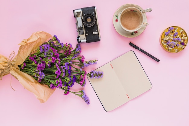 Bloemen boeket; vintage camera; dagboek; pen; koffiekopje en coaster op roze achtergrond