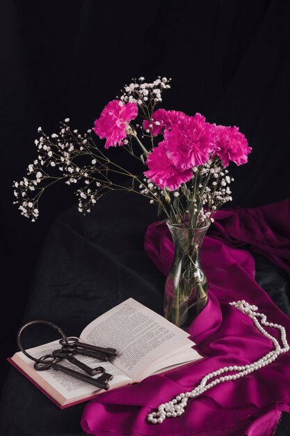 Bloemen met bloeitakjes in vaas dichtbij sleutels op volume en parels op purpere textiel in duisternis