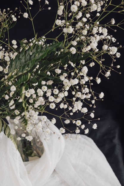 Bloemen met planten in vaas in de buurt van witte textiel