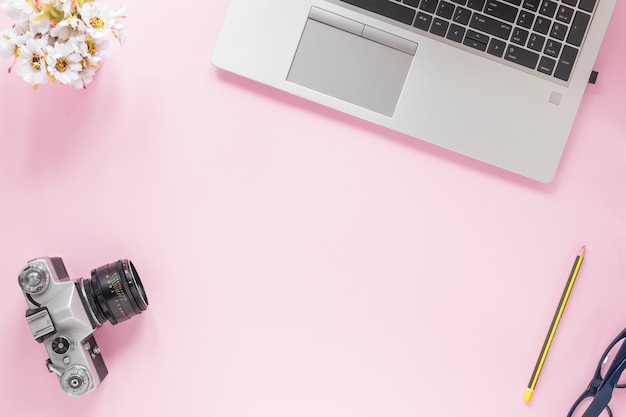 Bloemenvaas; camera; potlood; brillen en laptop op roze achtergrond