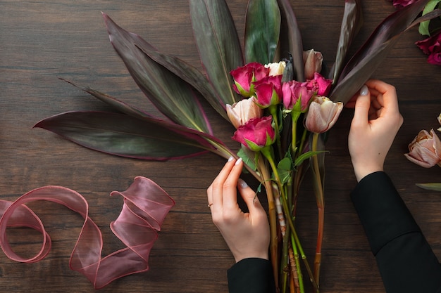 Bloemist op het werk: vrouw mode moderne boeket van verschillende bloemen op houten achtergrond maken. Masterclass. Cadeau voor bruid op bruiloft, moederdag, vrouwendag. Romantische lentemode. Passie rozen.