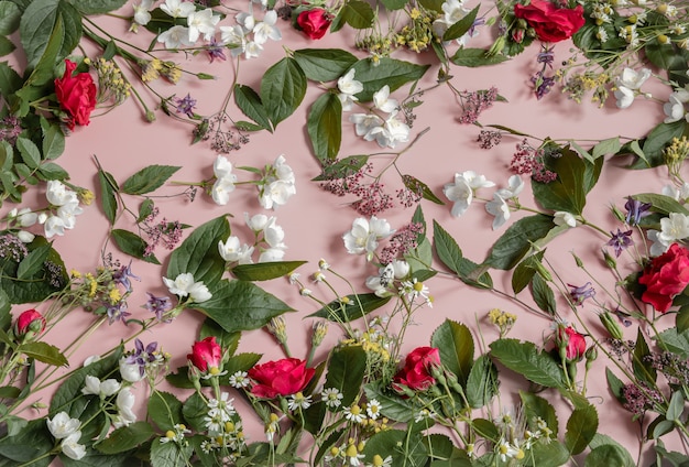 Bloemstuk met verschillende verse bloemen, bladeren en twijgen op een roze achtergrond.