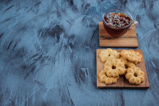 Bloemvormige zoete koekjes en glas kruidenthee op blauwe achtergrond.