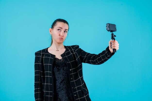 Blogger-meisje neemt selfie met minicamera door omhoog te kijken op een blauwe achtergrond