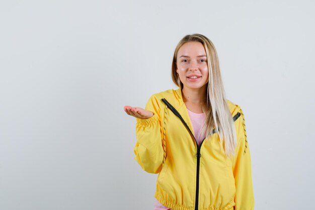 Blond meisje dat doet alsof ze iets in een gele jas vasthoudt en er vrolijk uitziet.