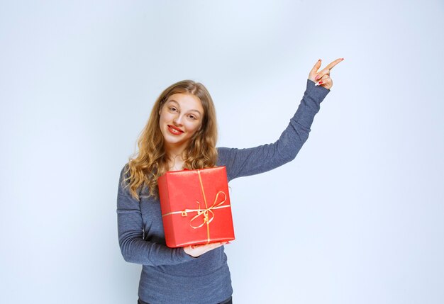 Blond meisje dat een rode geschenkdoos houdt en iemand laat zien.