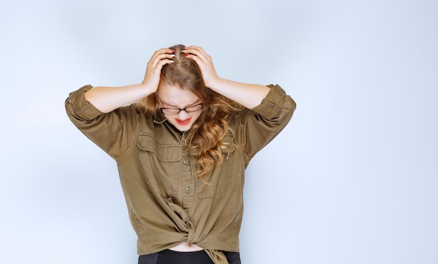 Gratis foto blond meisje dat haar hoofd vasthoudt, ziet er doodsbang en uitgeput uit.