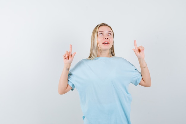 Blond meisje dat met wijsvingers in blauw t-shirt benadrukt en gelukkig kijkt. vooraanzicht.