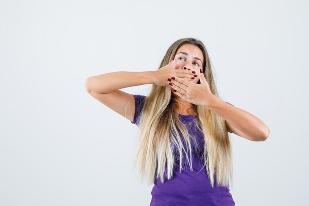 Blond meisje geeuwen en rekken in violet t-shirt en op zoek slaperig, vooraanzicht.