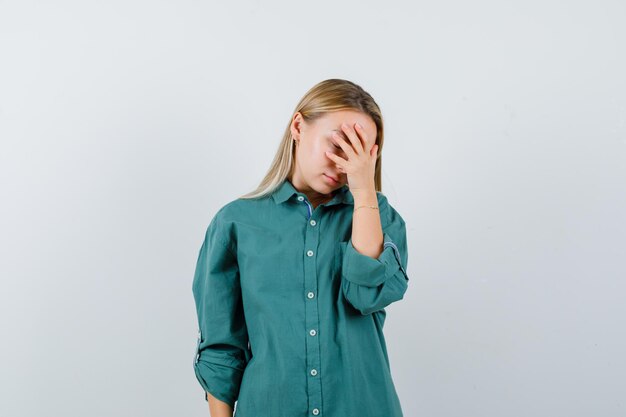 Blond meisje hand op oog in groene blouse zetten en moe kijken.