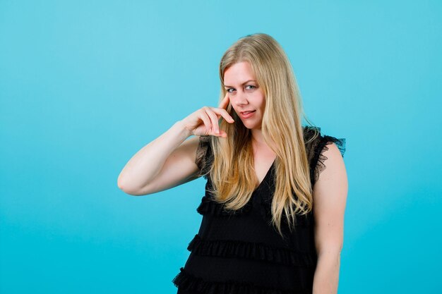 Blond meisje houdt wijsvinger op tempel op blauwe achtergrond