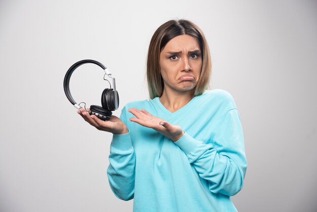 Blond meisje in blauw sweatshirt luistert naar de koptelefoon en geniet niet van de muziek.