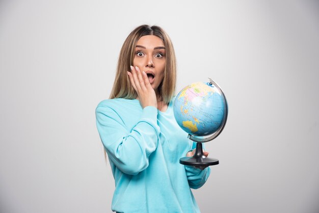 Blond meisje in blauw sweatshirt met een wereldbol en op zoek verrast.