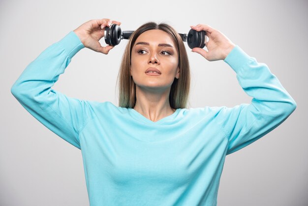 Blond meisje in blauw sweatshirt met koptelefoon en maakt zich klaar om ze te dragen om naar de muziek te luisteren.