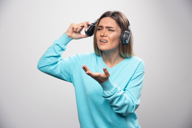 Blond meisje in blauw sweatshirt met koptelefoon om de mensen rond te horen.