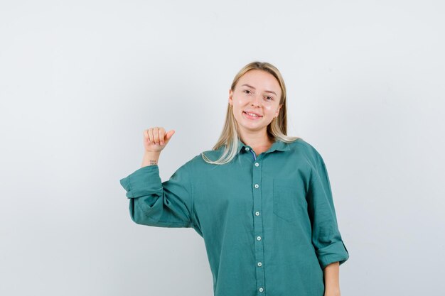 Blond meisje in een groene blouse die de vuist balt en er gelukkig uitziet