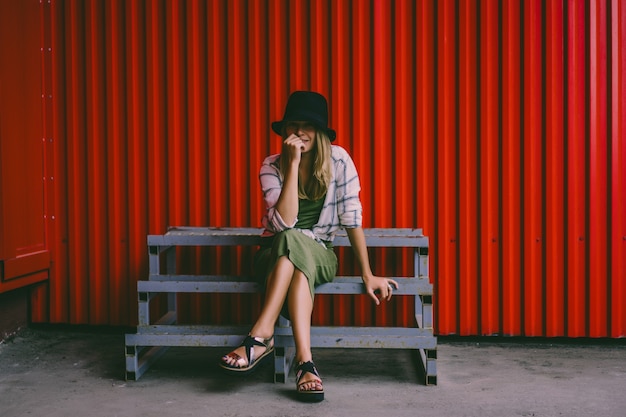 Blond meisje in een hoed. Straatfoto. Een mooi meisje dat casual kleding draagt, lacht mysterieus. Vintage-stijl