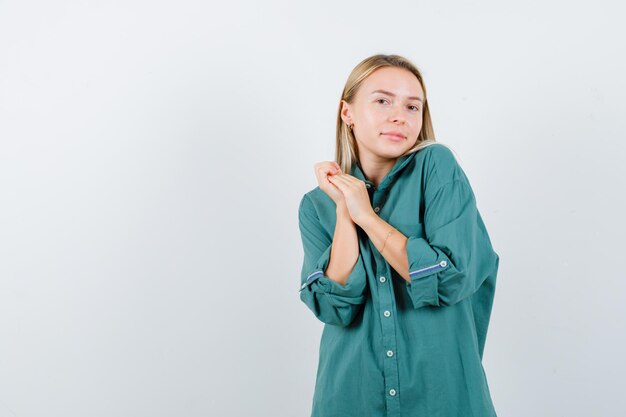 Blond meisje in groene blouse die handen omklemt en er betoverend uitziet