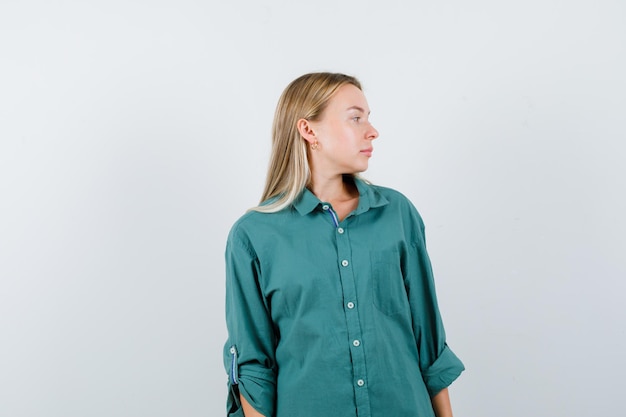 Blond meisje in groene blouse kijkt weg terwijl ze voor de camera poseert en er betoverend uitziet