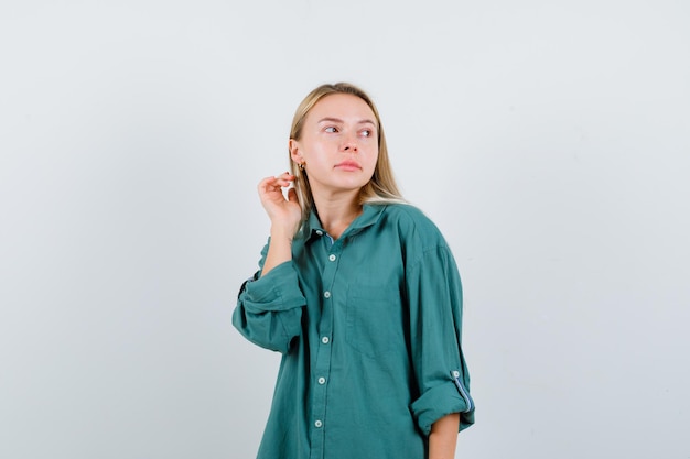 Blond meisje in groene blouse kijkt weg terwijl ze voor de camera poseert en er betoverend uitziet