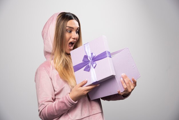 Blond meisje in sweatshirt ontving een geschenkdoos en voelt zich positief verrast.