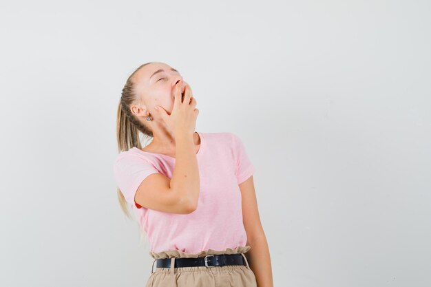 Blond meisje in t-shirt, broek geeuwen en op zoek slaperig, vooraanzicht.