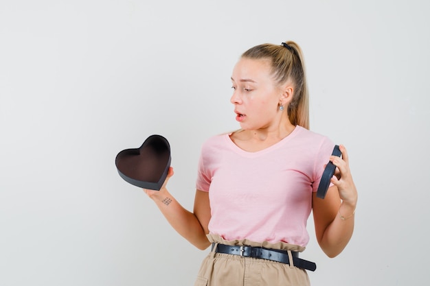 Blond meisje in t-shirt, broek kijken naar lege geschenkdoos en op zoek verrast, vooraanzicht.