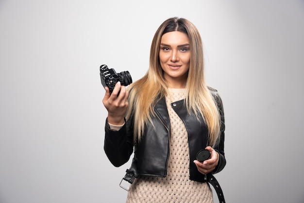 Blond meisje in zwart leren jasje dat haar selfies met een camera neemt.