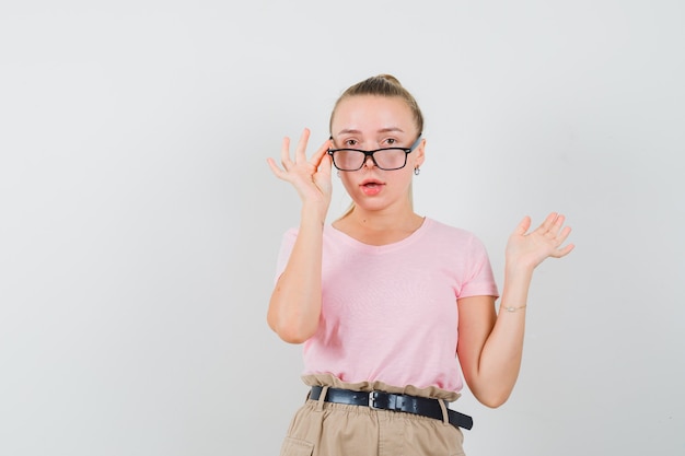 Blond meisje kijkt naar voorkant in t-shirt, broek en kijkt verbaasd.