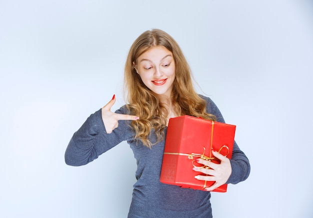 Blond meisje knuffelt haar rode geschenkdoos en voelt zich gelukkig.