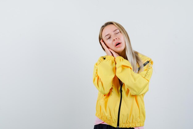 Blond meisje leunend op handpalmen als kussen in t-shirt, jas en ziet er schattig uit