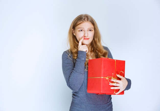 Blond meisje met een rode geschenkdoos ziet er attent en moe uit.