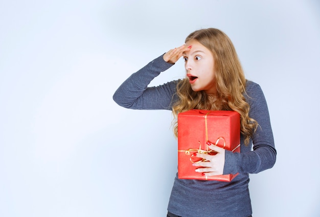 Blond meisje met een rode geschenkdoos ziet er verward en doodsbang uit.