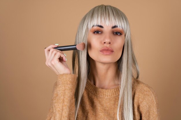 Blond meisje met pony en bruine make-up voor overdag houdt een borstel vast voor blush-contouren en markeerstift