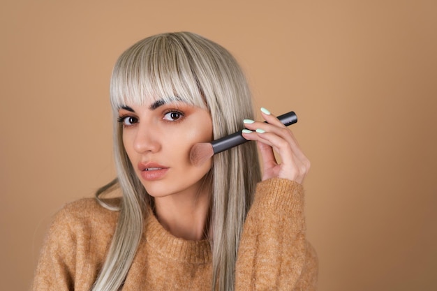 Gratis foto blond meisje met pony en bruine make-up voor overdag houdt een borstel vast voor blush-contouren en markeerstift