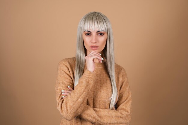 Blond meisje met pony en bruine make-up voor overdag in een trui op beige achtergrond sensueel modeportret