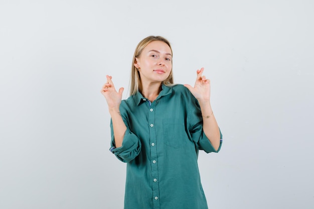 Blond meisje staande vingers gekruist in groene blouse en ziet er mooi uit.