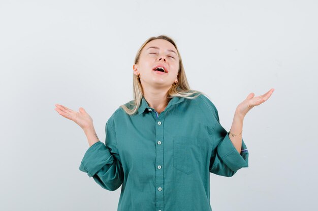 Blond meisje strekt haar handen op vragende manier uit in een groene blouse en ziet er gelukkig uit.