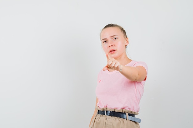 Blond wijfje dat naar voren in t-shirt, broek richt en er zelfverzekerd uitziet. vooraanzicht.