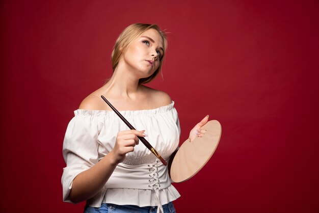 Blonde artiest houdt een palet en borstels vast en ziet er geconcentreerd en gefocust uit op haar werk.