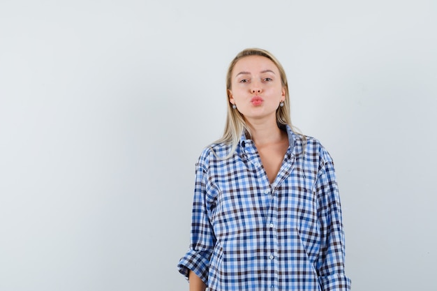 Blonde dame die de lippen gevouwen houdt in een geruit overhemd en er aardig uitziet