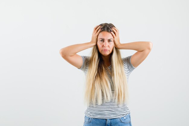 Blonde dame die hand op haar hoofd in t-shirt houdt en ongelukkig kijkt. vooraanzicht.