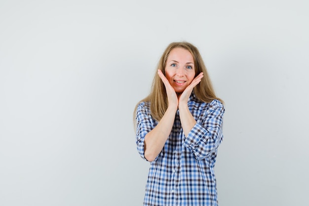 Blonde dame die handpalmen onder de kin in overhemd houdt en er schattig uitziet.