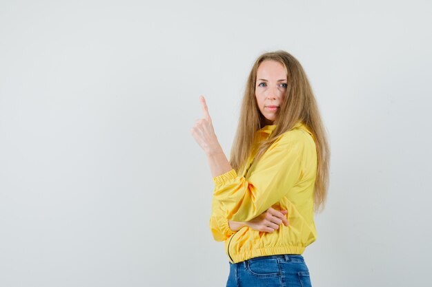 Blonde dame die in jas, jeans benadrukt en er zelfverzekerd uitziet.