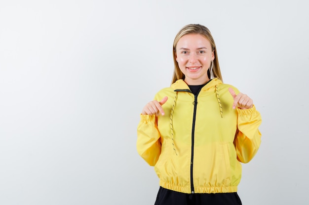 Blonde dame die in trainingspak naar beneden wijst en vreugdevol kijkt. vooraanzicht.