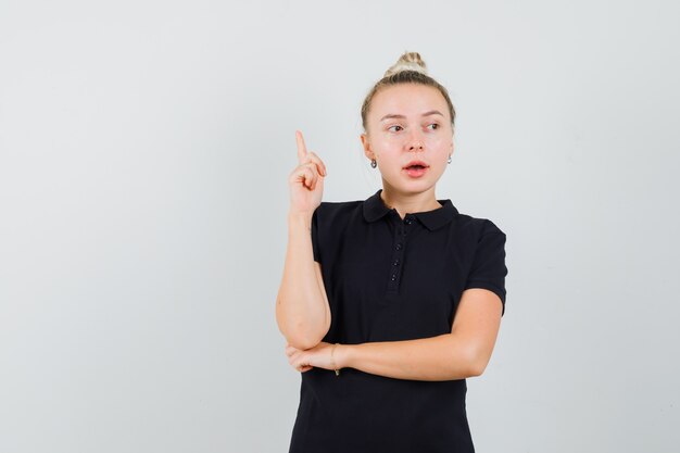 Blonde dame die omhoog wijst terwijl opzij in zwart t-shirt, vooraanzicht kijkt.