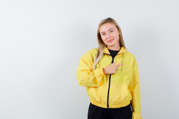 Blonde dame die recht in trainingspak wijst en er vrolijk uitziet, vooraanzicht.