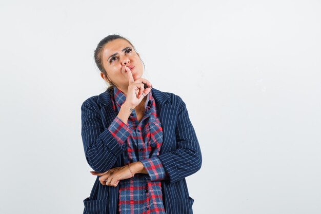 Blonde dame die vinger op lippen houdt terwijl het opzoeken in overhemd, jasje vooraanzicht.